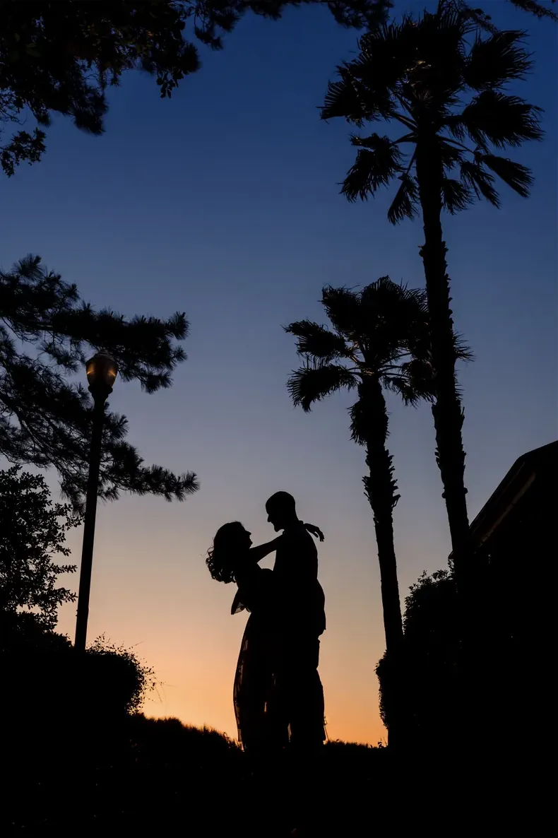 Couple silhouetted under palms at dusk